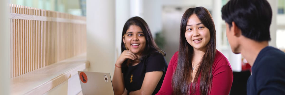 Three students talk in the Management School hub.